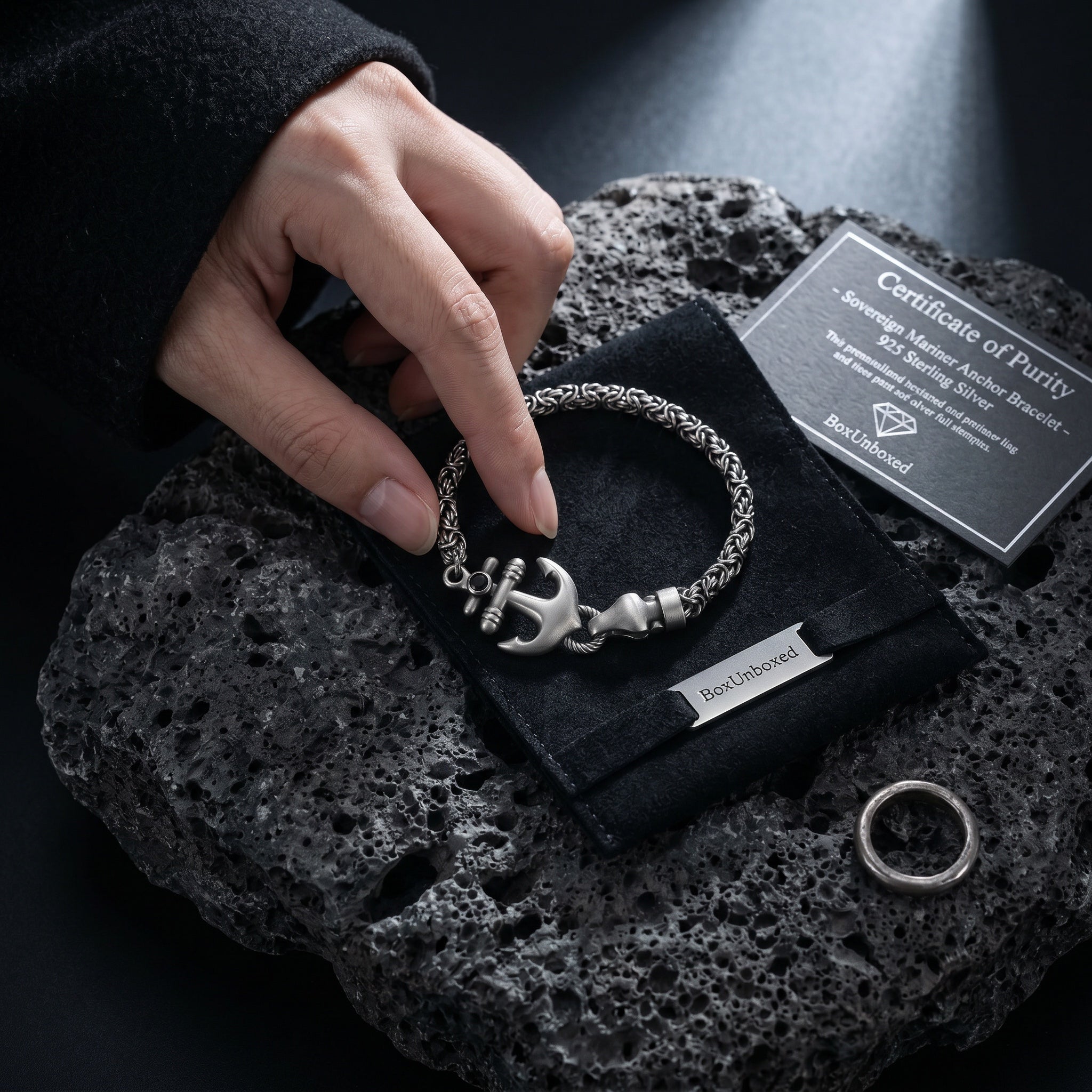 Silver bracelet with anchor charm on a black fabric with 'Best Unlimited' branding, displayed on a dark textured surface.