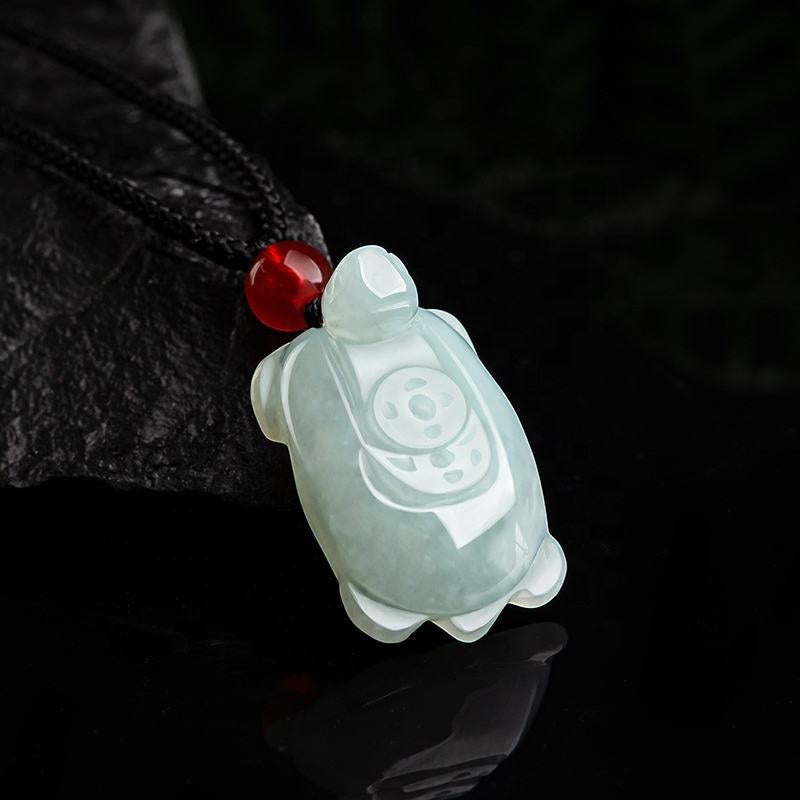 BoxUnboxed hand-carved natural jadeite turtle pendant with a red bead on a black cord against a dark background
