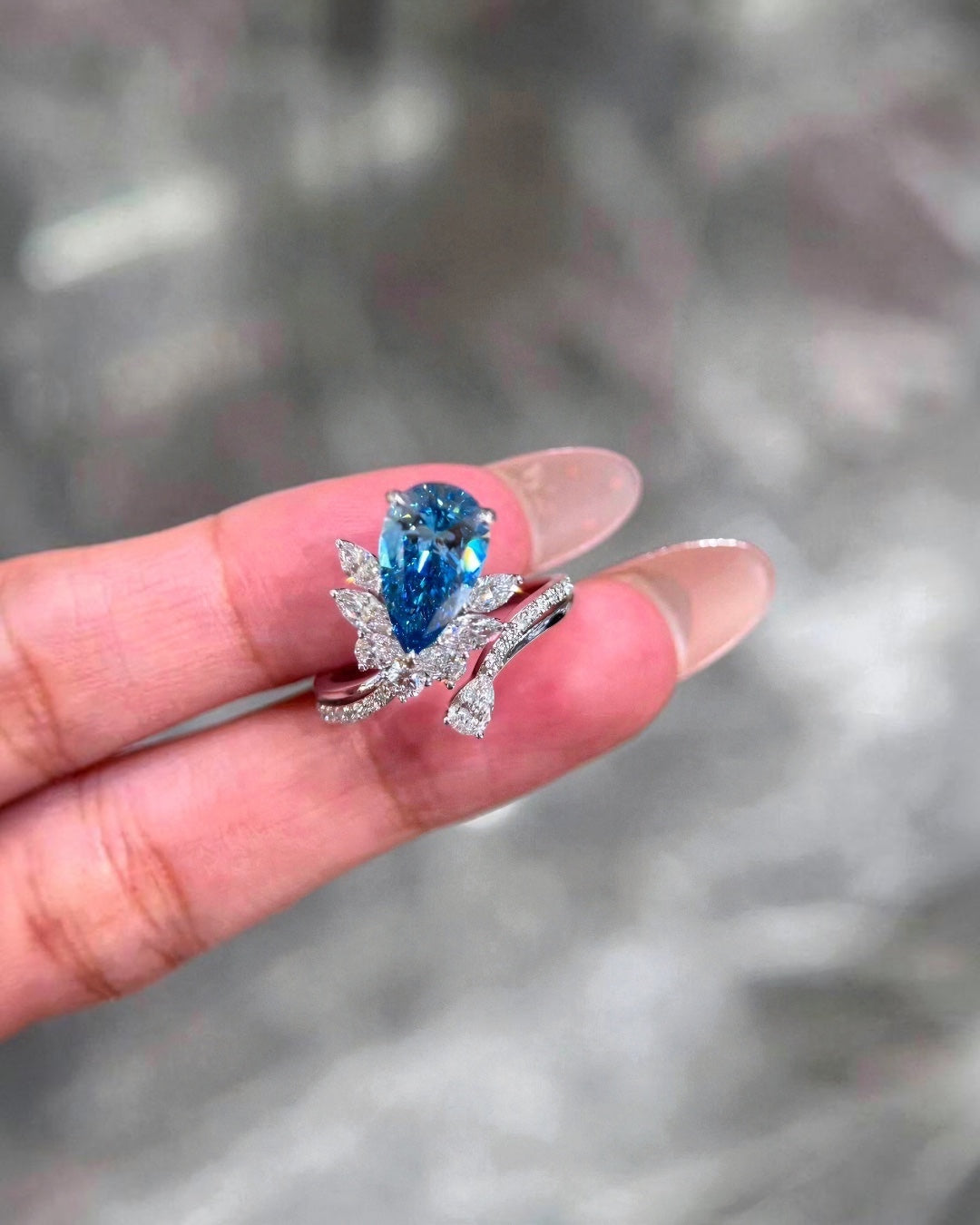 BoxUnboxed pear-cut vivid blue lab-grown diamond ring with floral-inspired diamond accents in a polished metal setting.